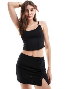 a woman in a black top and skirt posing for the camera with her hand on her head