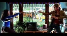 two women are dancing in front of a tv screen and windows with cars behind them