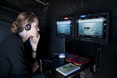 a woman sitting in front of two monitors with headphones on and looking at the screen