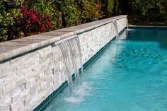 a pool with a waterfall running down it's side next to a brick wall