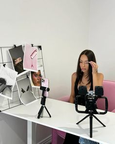 a woman sitting at a desk with a camera and tripod in front of her