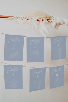 wedding seating cards hanging from a string on a white wall in front of a feather