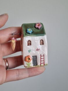 a hand holding a tiny toy house made out of clay