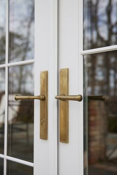 a close up of a door handle on a white door with glass panes and trees in the background