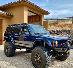 a blue jeep is parked in front of a house with rocks and gravel around it