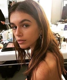 a woman with long brown hair is sitting in front of a mirror and looking at the camera