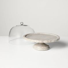 a cake stand with a glass dome on top and a stone base underneath it, sitting on a white surface