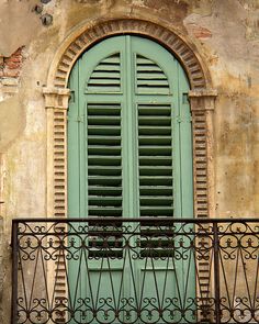 an iron balcony railing with shutters and green doors