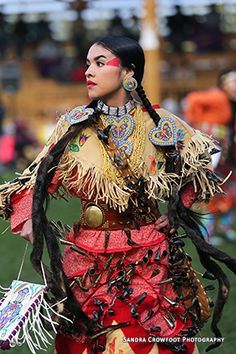 a woman dressed in native garb walking on the grass with other people behind her