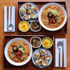 two trays filled with different types of food on top of a wooden table next to utensils