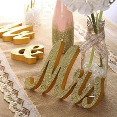 two vases with flowers in them sitting on a burlap table cloth next to wooden letters