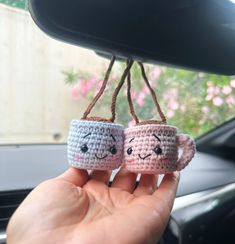 two crocheted coffee mugs hanging from a car dashboard