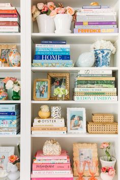 a white bookcase filled with lots of books next to vases and flowers on top of each shelf