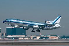 a blue and white jet airliner taking off from an airport runway with buildings in the background