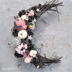 a wreath made out of branches with flowers and balls on the top, sitting on concrete