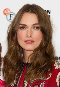 a woman with long brown hair wearing a red dress and posing for the camera at an event