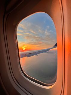 an airplane window with the sun setting in the sky over water and land behind it