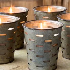 four metal buckets filled with candles sitting on top of a wooden table next to each other