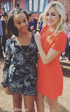 two young women standing next to each other in front of a crowd at an outdoor event