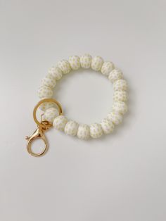 a white and gold beaded keychain on a white table with a pair of scissors