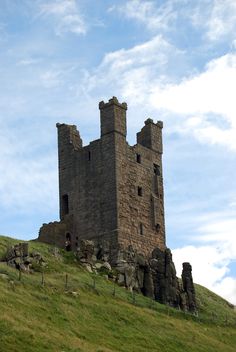 an old castle sitting on top of a lush green hillside under a blue cloudy sky