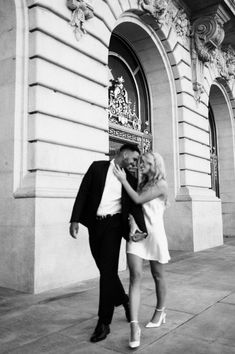 black and white photograph of a couple kissing in front of an ornate building with columns