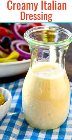 a jar filled with creamy italian dressing next to a bowl of olives and peppers