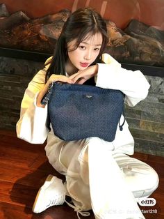 a woman sitting on the floor with her handbag in front of her face and looking at the camera