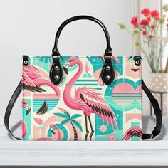 a pink flamingo print purse sitting on top of a white table next to a vase with red flowers