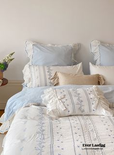 a bed with blue and white linens in a bedroom next to a plant on a table