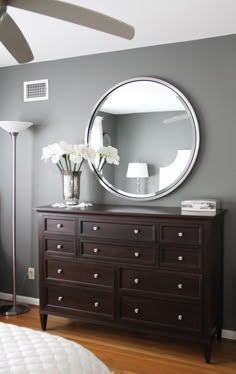 a bedroom with a dresser, mirror and lamp on the side wall in front of a bed