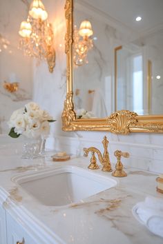 a bathroom with marble counter tops and gold framed mirror above the sink, surrounded by white flowers