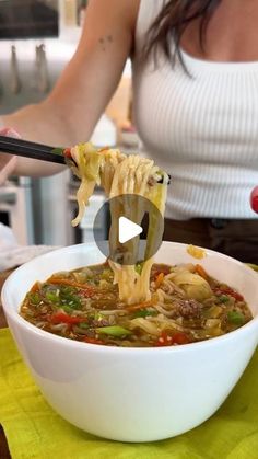 a woman is holding chopsticks over a bowl of soup with noodles and vegetables