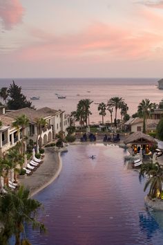 an outdoor swimming pool surrounded by palm trees next to the ocean with boats in the water