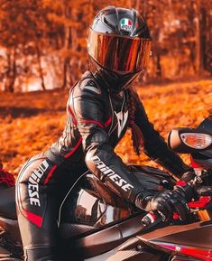 a person wearing a helmet sitting on a motor bike in the fall leaves with trees behind them