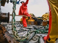 a man in red is standing on the deck of a boat with ropes and rope