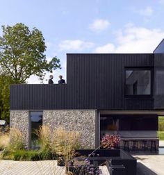 two people are standing on the roof of a house with black siding and stone walls