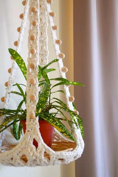 a crocheted plant hanger with a potted plant in the middle, hanging from it's side