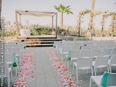 an outdoor ceremony set up with white chairs and rose petals