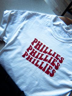 "A cute, simple short sleeve shirt - This is for the \"Philadelphia Phillies\" but, I can make this for any sports team. Just send me which team you would like in the personalization box." Red T-shirt With Name Print For Game Day, Game Day Red T-shirt With Name Print, Collegiate Name Print T-shirt For Fans, Red T-shirt With Name Print For Sports Events, Red Name Print T-shirt For Game Day, Red Name Print T-shirt For Sports Events, White School Spirit T-shirt With Name Print, White T-shirt With Name Print For Game Day, Fan Merchandise T-shirt With Name Print