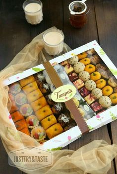 an assortment of pastries in a box on top of a wooden table next to two cups of coffee