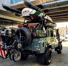 an army green jeep parked in front of a building with kayaks on it's roof