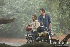 a man and woman standing in the rain next to a motorcycle with a helmet on it