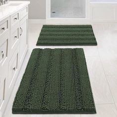 two green rugs sitting on top of a bathroom floor next to a bath tub