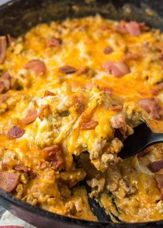 a skillet filled with ham and cheese on top of a striped table cloth next to a wooden spoon