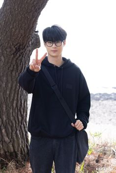 a young man standing next to a tree giving the peace sign with his hand in front of him