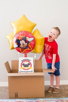 a young boy standing in front of a box with balloons and a mickey mouse balloon