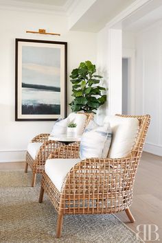 two wicker chairs sitting next to each other in front of a painting on the wall