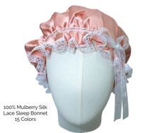 a white mannequin head wearing a pink satin bonnet with lace trim and bows