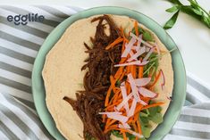 a tortilla topped with shredded carrots and beef on top of a blue plate